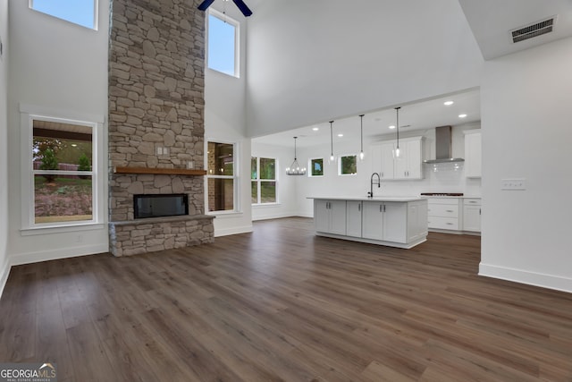 unfurnished living room with a stone fireplace, a towering ceiling, a wealth of natural light, and dark hardwood / wood-style floors