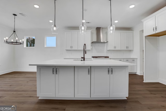 kitchen featuring dark hardwood / wood-style flooring, a center island with sink, white cabinets, wall chimney range hood, and decorative light fixtures