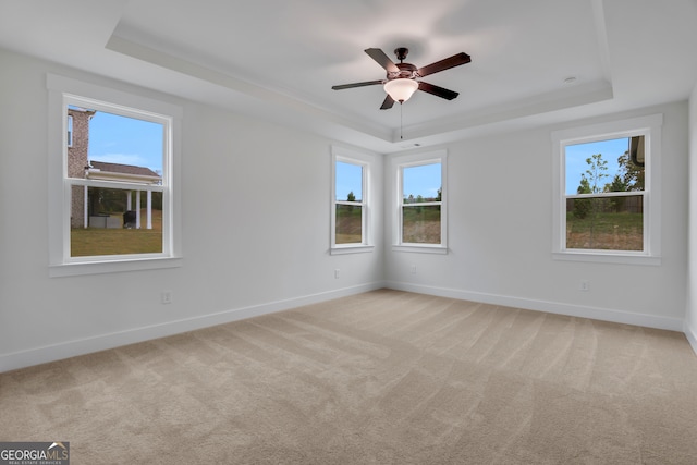 carpeted empty room with a wealth of natural light, ceiling fan, and a raised ceiling