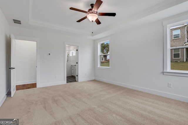 unfurnished bedroom with ensuite bathroom, light carpet, a raised ceiling, and ceiling fan