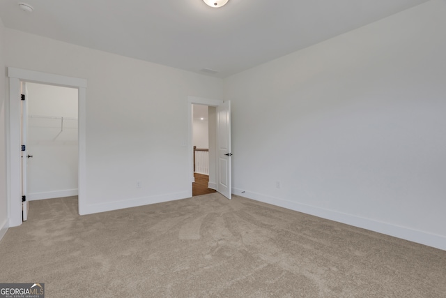 unfurnished bedroom with a spacious closet, light colored carpet, and a closet