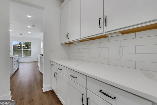 interior space with wood-type flooring, light stone counters, white cabinets, a notable chandelier, and pendant lighting