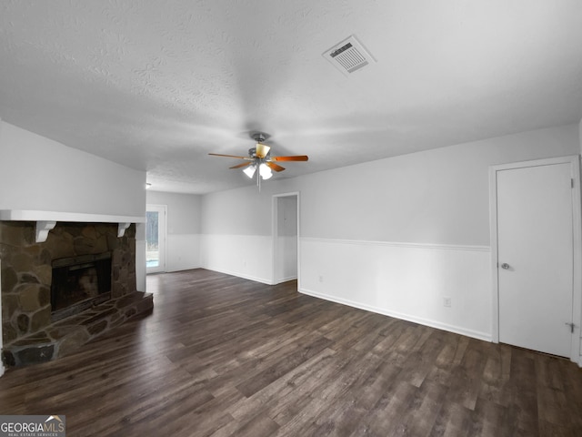 unfurnished living room featuring a textured ceiling, a fireplace, visible vents, a ceiling fan, and dark wood-style floors