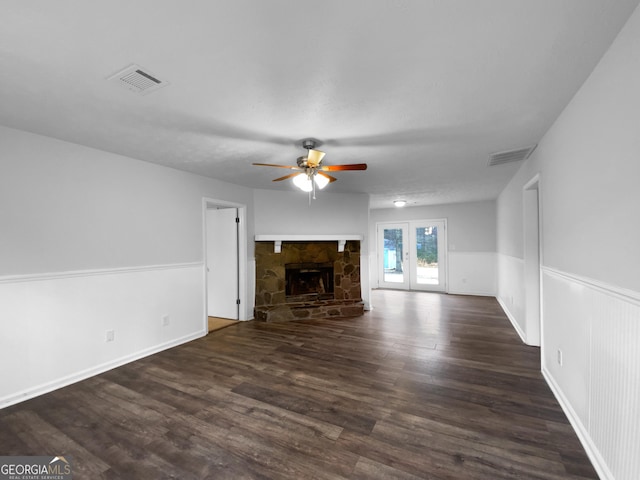 unfurnished living room featuring a ceiling fan, visible vents, dark wood finished floors, and a stone fireplace