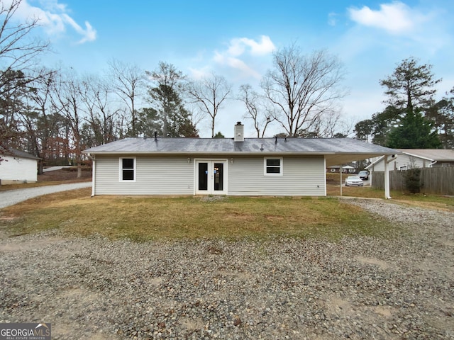 back of house featuring gravel driveway, french doors, a yard, a chimney, and a carport