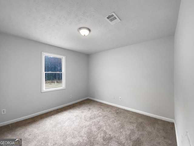 spare room featuring carpet, visible vents, a textured ceiling, and baseboards