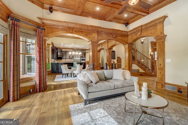 living room featuring crown molding, light hardwood / wood-style floors, coffered ceiling, ornate columns, and ceiling fan with notable chandelier