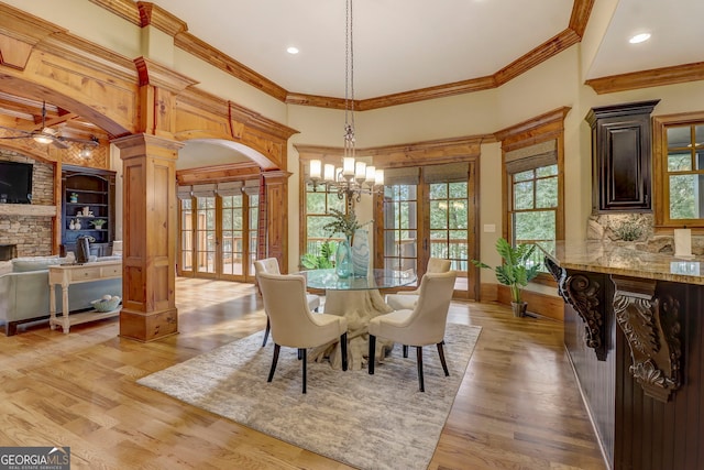 dining area with light hardwood / wood-style floors, a fireplace, ceiling fan with notable chandelier, ornamental molding, and decorative columns