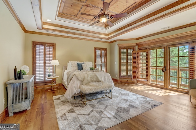 bedroom featuring a raised ceiling, ornamental molding, multiple windows, and light wood-type flooring