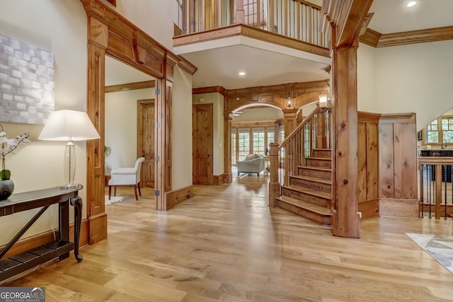 foyer featuring a towering ceiling, decorative columns, light wood-type flooring, and crown molding