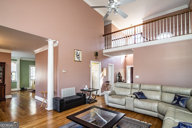 living room with ceiling fan, crown molding, decorative columns, dark wood-type flooring, and a high ceiling