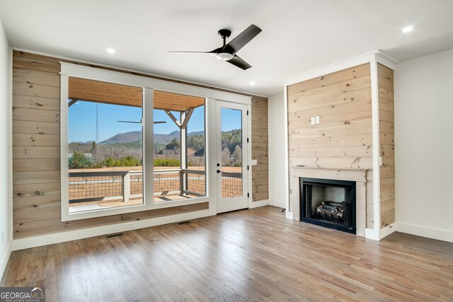 unfurnished living room featuring ceiling fan, light wood-type flooring, and wooden walls