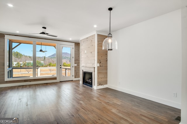 unfurnished living room with wooden walls, a large fireplace, ceiling fan, and dark hardwood / wood-style flooring