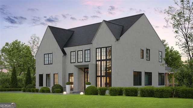 back of house at dusk with stucco siding and a yard