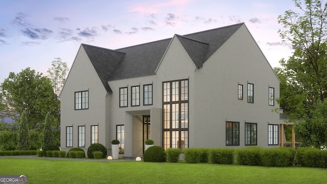 back of property at dusk featuring a lawn and stucco siding