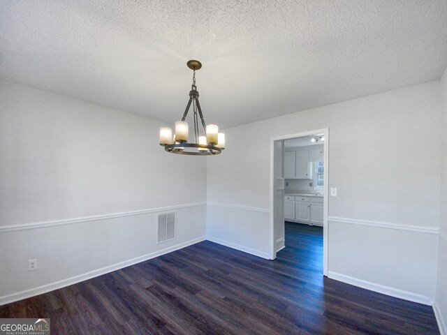 spare room featuring dark hardwood / wood-style floors, a textured ceiling, and a notable chandelier