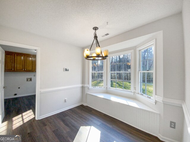 unfurnished dining area featuring dark wood-type flooring, a textured ceiling, a chandelier, and plenty of natural light