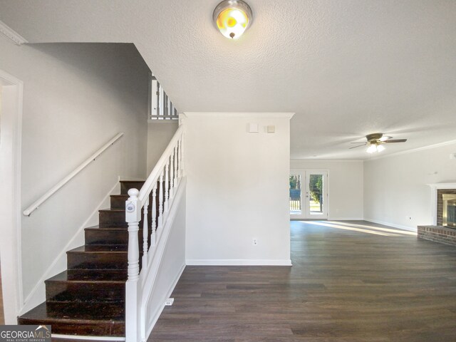 stairs featuring crown molding, ceiling fan, a textured ceiling, a brick fireplace, and dark hardwood / wood-style floors