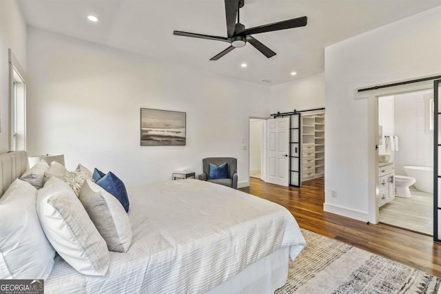 bedroom with a barn door, dark hardwood / wood-style floors, ceiling fan, and connected bathroom