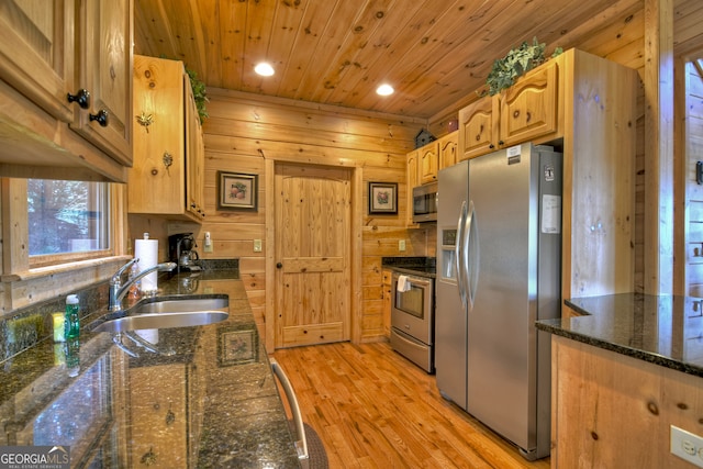 kitchen with appliances with stainless steel finishes, wood walls, dark stone countertops, light hardwood / wood-style floors, and sink