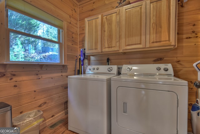 washroom featuring wooden walls, washing machine and clothes dryer, and cabinets