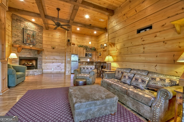 living room featuring light wood-type flooring, a stone fireplace, ceiling fan, wooden ceiling, and beamed ceiling