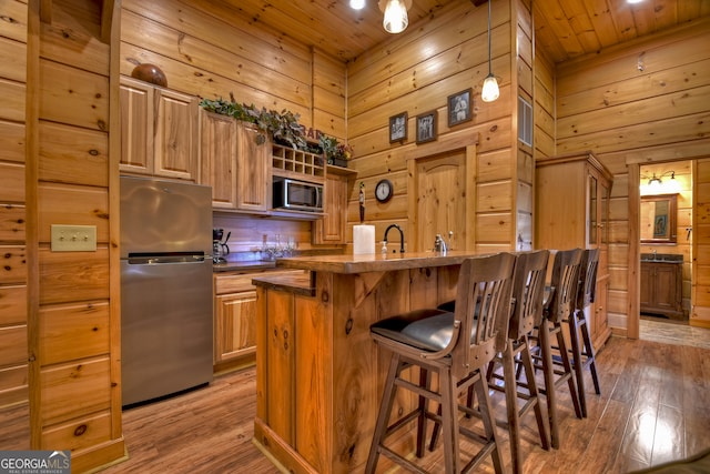 kitchen featuring wooden walls, a kitchen breakfast bar, wooden ceiling, light wood-type flooring, and appliances with stainless steel finishes