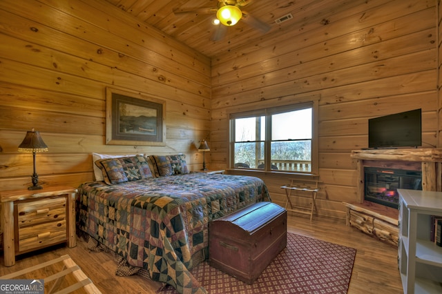 bedroom with wooden walls, a stone fireplace, light hardwood / wood-style floors, and ceiling fan