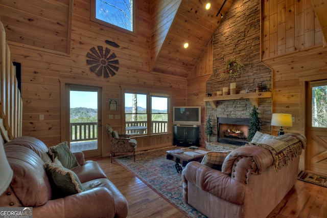 living room with a stone fireplace, wooden ceiling, light wood-type flooring, high vaulted ceiling, and wood walls