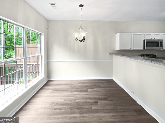 unfurnished dining area featuring baseboards, visible vents, wood finished floors, and a notable chandelier