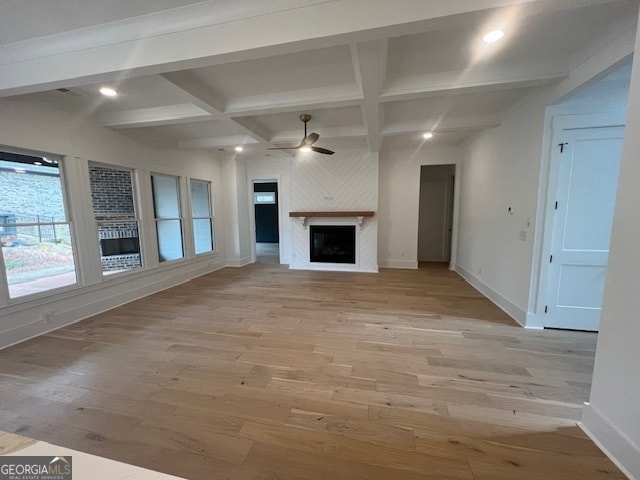 unfurnished living room with coffered ceiling, a large fireplace, ceiling fan, beamed ceiling, and light wood-type flooring