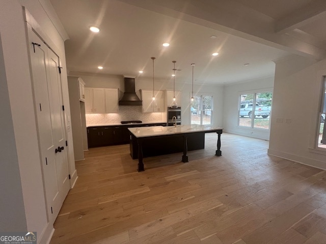 kitchen with custom range hood, an island with sink, light hardwood / wood-style floors, and decorative light fixtures