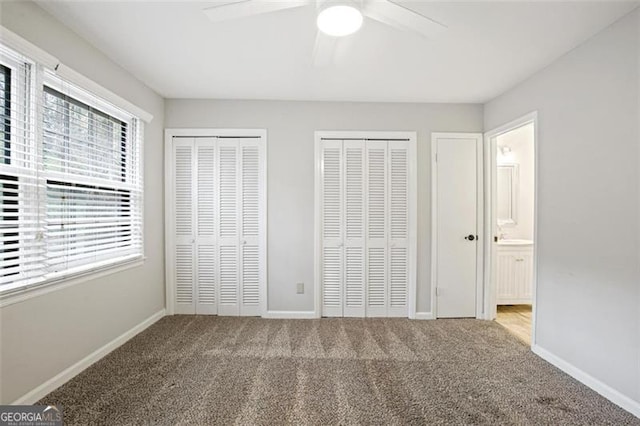 unfurnished bedroom with ensuite bath, two closets, ceiling fan, and carpet floors