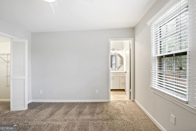 unfurnished bedroom featuring a walk in closet, a closet, ensuite bathroom, light carpet, and ceiling fan