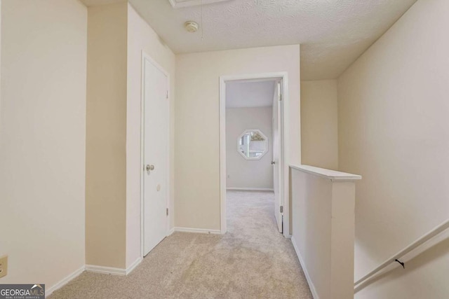 hallway with a textured ceiling and light carpet