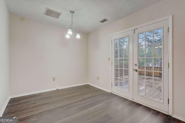 spare room with a chandelier, french doors, a textured ceiling, and dark wood-type flooring