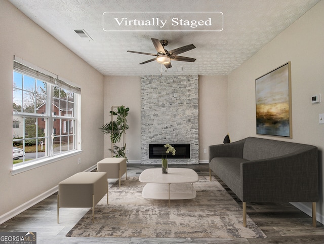 living room featuring a fireplace, a textured ceiling, dark wood-type flooring, and ceiling fan