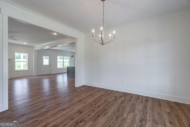 empty room featuring an inviting chandelier, dark hardwood / wood-style flooring, and crown molding