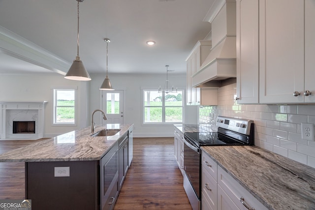 kitchen featuring pendant lighting, custom exhaust hood, sink, stainless steel electric range oven, and an island with sink