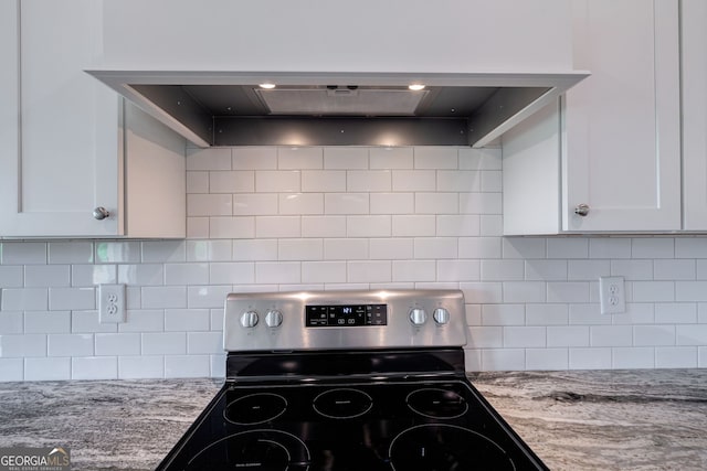 kitchen with backsplash, wall chimney range hood, stainless steel range with electric stovetop, white cabinets, and light stone counters