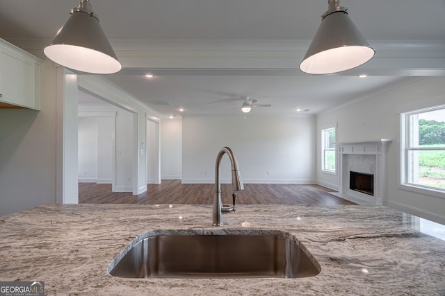 kitchen with decorative light fixtures, a fireplace, sink, crown molding, and light stone counters