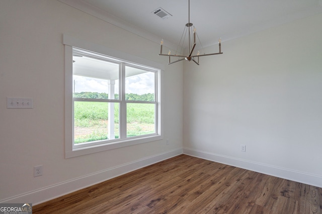 spare room featuring dark hardwood / wood-style flooring, ornamental molding, and a notable chandelier