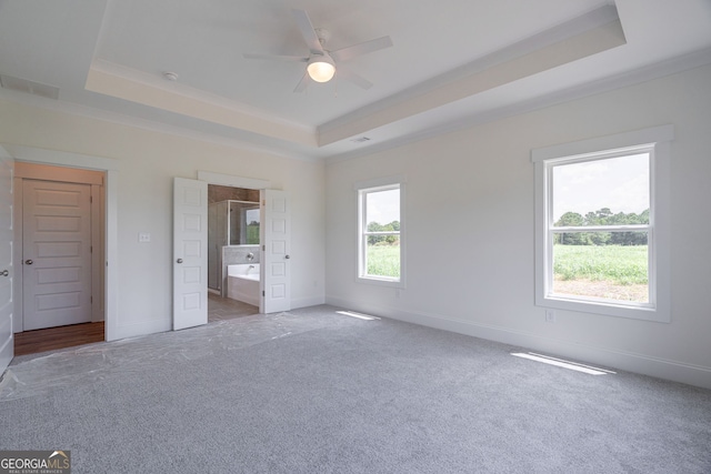 unfurnished bedroom featuring ceiling fan, light colored carpet, a tray ceiling, and ensuite bath