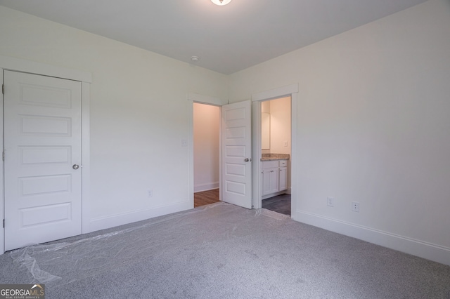 unfurnished bedroom featuring dark colored carpet, a closet, and connected bathroom