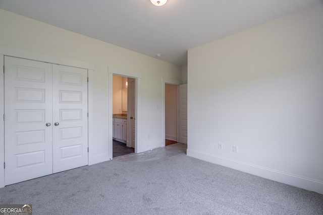 unfurnished bedroom featuring a closet, ensuite bathroom, and dark carpet