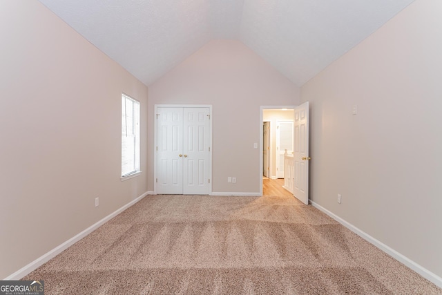 unfurnished bedroom featuring light colored carpet, lofted ceiling, and a closet