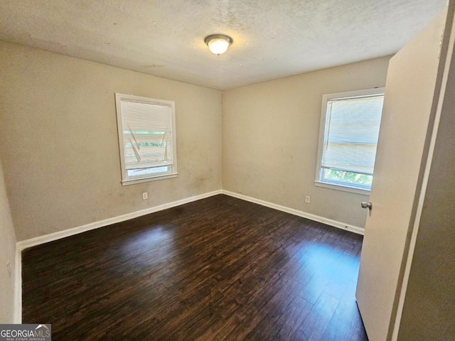 empty room with dark hardwood / wood-style flooring, a textured ceiling, and a healthy amount of sunlight