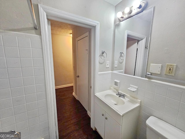 bathroom with toilet, vanity, tile walls, and hardwood / wood-style floors