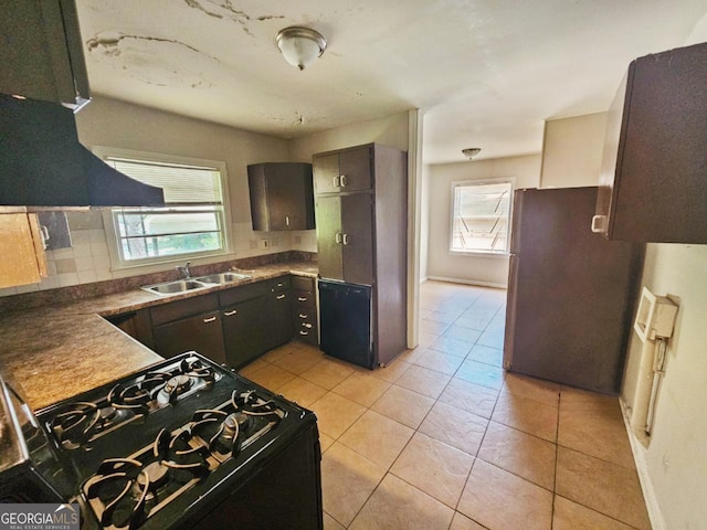 kitchen with sink, light tile patterned floors, decorative backsplash, stainless steel fridge, and black gas range oven