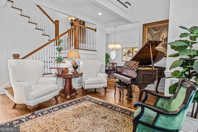 sitting room featuring wood-type flooring, a towering ceiling, ornamental molding, and an inviting chandelier